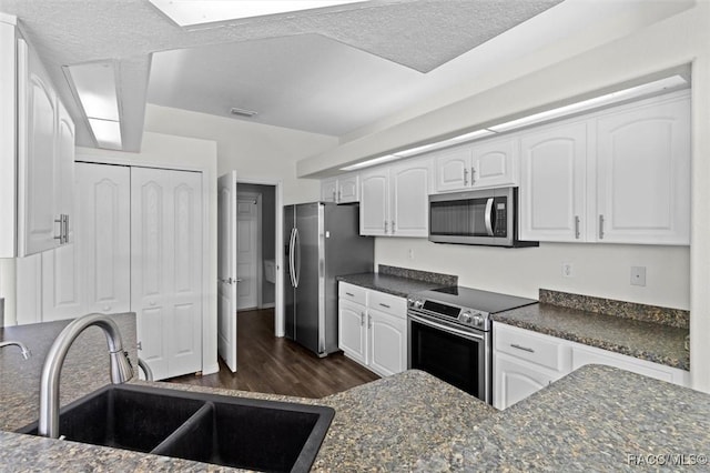 kitchen featuring a textured ceiling, white cabinets, a sink, dark wood finished floors, and appliances with stainless steel finishes
