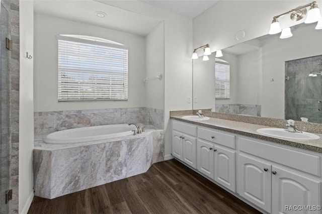 bathroom featuring wood finished floors, a sink, a bath, and a stall shower