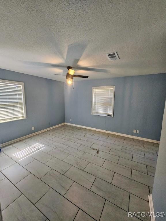 tiled empty room with ceiling fan and a textured ceiling