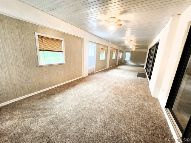 unfurnished living room featuring carpet, ceiling fan, and wood walls