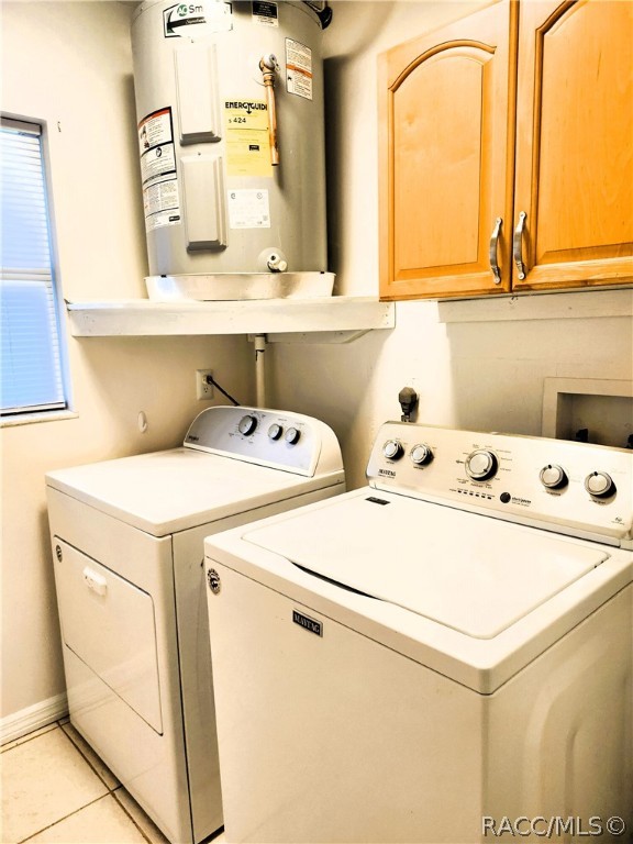 clothes washing area featuring washing machine and clothes dryer, electric water heater, light tile patterned floors, and cabinets