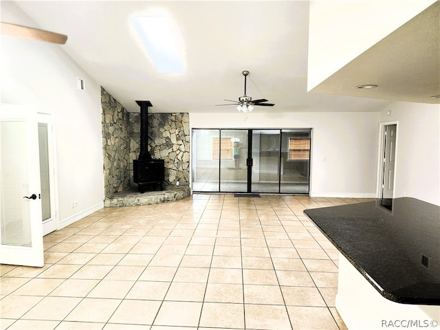 unfurnished living room featuring a wood stove, ceiling fan, and light tile patterned floors