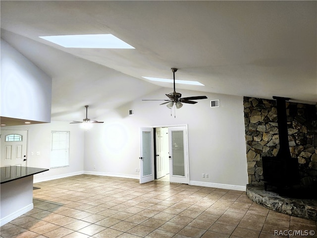 unfurnished living room with high vaulted ceiling, a skylight, a wood stove, and ceiling fan