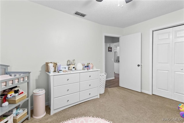 carpeted bedroom with a nursery area, a textured ceiling, ceiling fan, and a closet