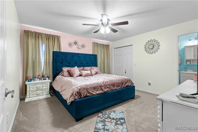 bedroom with a textured ceiling, a closet, connected bathroom, light colored carpet, and ceiling fan