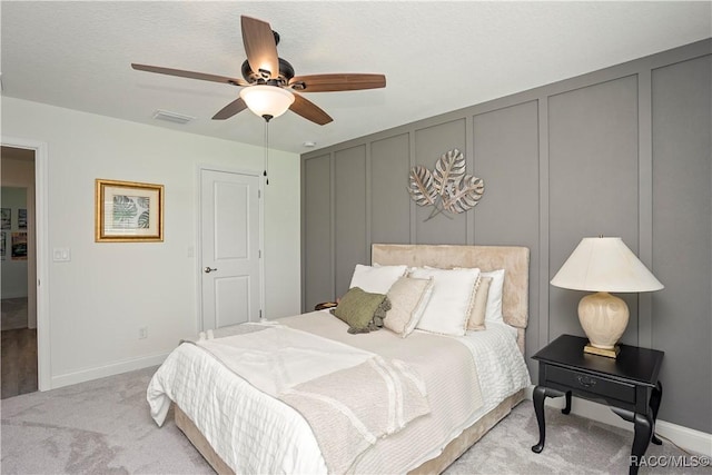 bedroom with baseboards, visible vents, carpet floors, ceiling fan, and a decorative wall