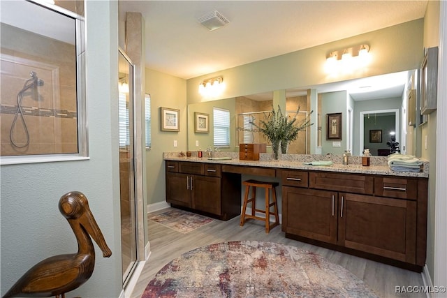 bathroom featuring visible vents, a shower stall, baseboards, double vanity, and wood finished floors