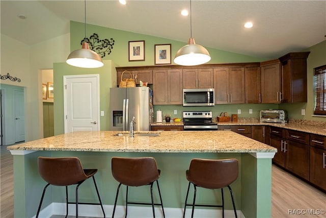 kitchen with decorative light fixtures, stainless steel appliances, a kitchen breakfast bar, and an island with sink