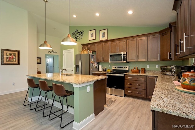 kitchen featuring a breakfast bar, a kitchen island with sink, light wood-style floors, appliances with stainless steel finishes, and light stone countertops