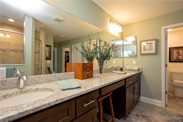 full bathroom featuring baseboards, toilet, double vanity, a stall shower, and a sink