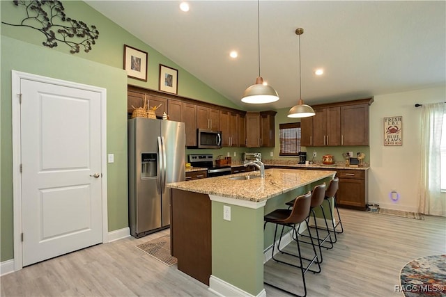 kitchen featuring a breakfast bar, a center island with sink, a sink, stainless steel appliances, and light wood finished floors