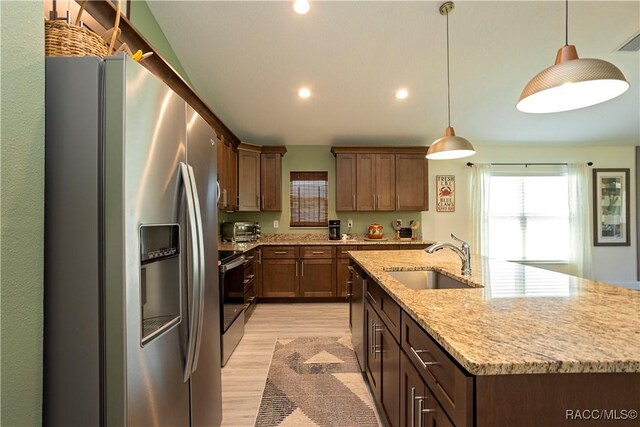 kitchen with light stone countertops, light wood finished floors, a sink, appliances with stainless steel finishes, and decorative light fixtures