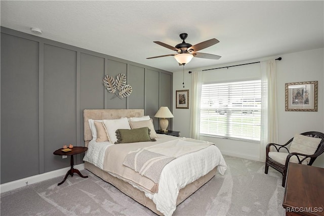 bedroom with a decorative wall, a ceiling fan, and light carpet