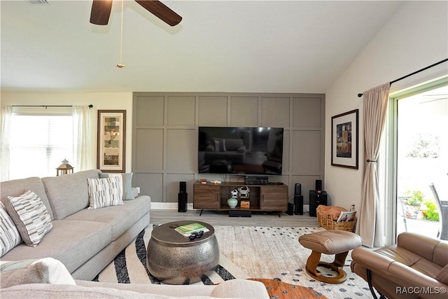 living area featuring light wood-type flooring, visible vents, a decorative wall, lofted ceiling, and ceiling fan