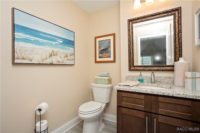 half bathroom with baseboards, toilet, and vanity