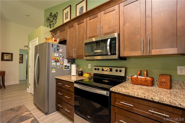 kitchen with light wood finished floors, appliances with stainless steel finishes, baseboards, and light stone countertops