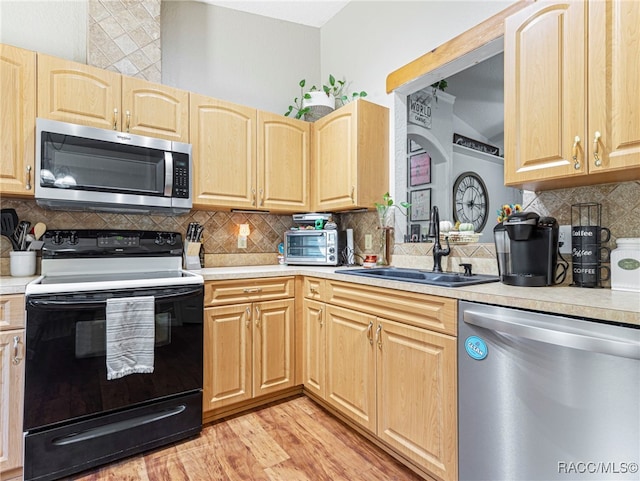 kitchen with decorative backsplash, appliances with stainless steel finishes, light brown cabinetry, sink, and light hardwood / wood-style floors