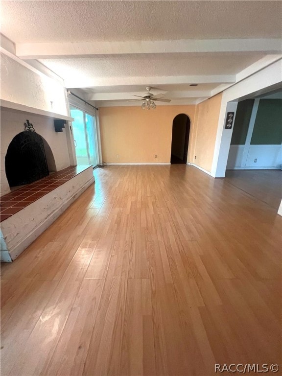 unfurnished living room with beamed ceiling, hardwood / wood-style floors, a textured ceiling, and ceiling fan