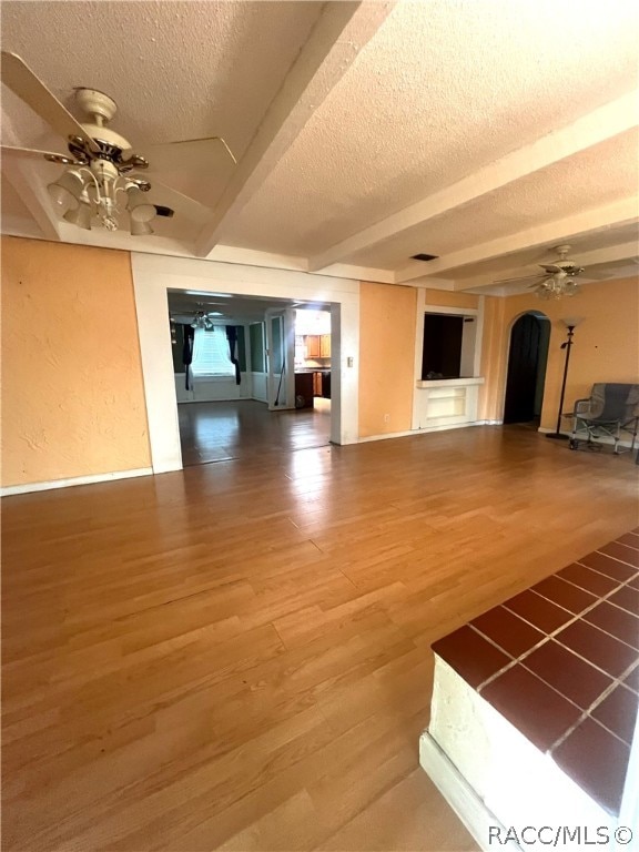 unfurnished living room with beam ceiling, ceiling fan, hardwood / wood-style floors, and a textured ceiling