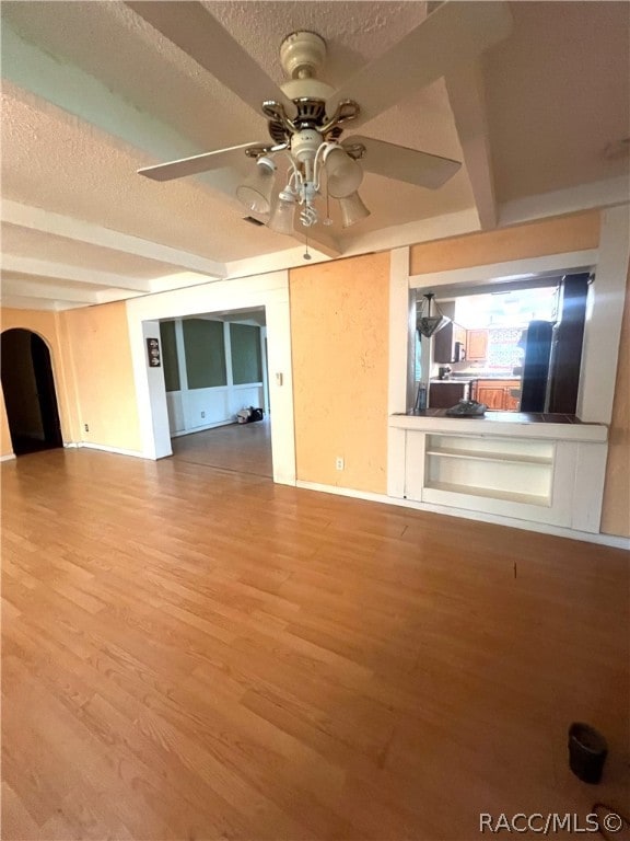 unfurnished living room with beam ceiling, ceiling fan, light hardwood / wood-style flooring, and a textured ceiling