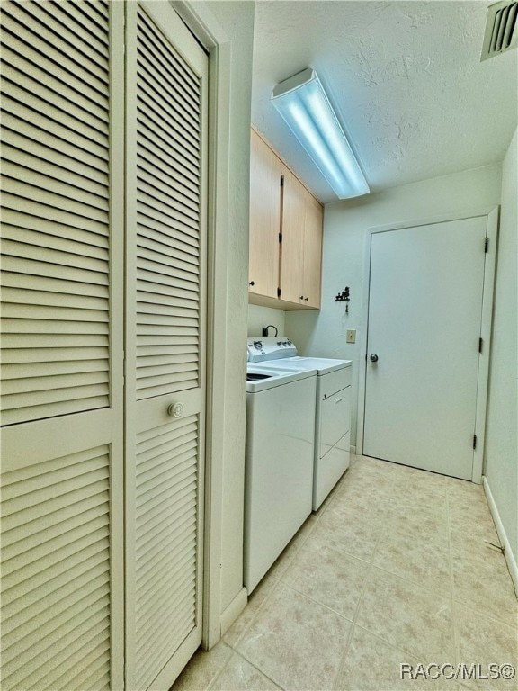 washroom featuring washing machine and dryer, light tile patterned floors, and cabinets