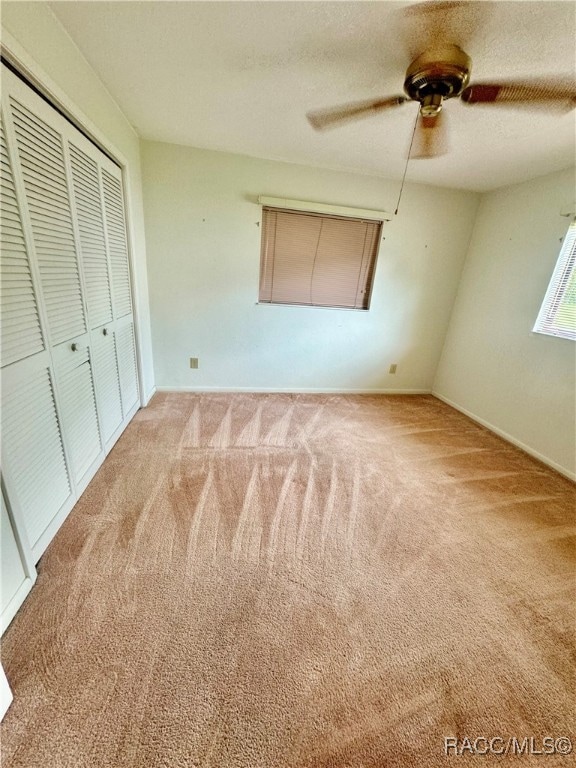 unfurnished bedroom with a closet, light colored carpet, and ceiling fan