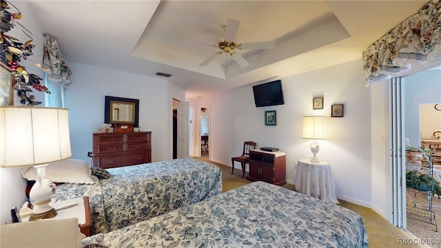 carpeted bedroom with ceiling fan and a tray ceiling