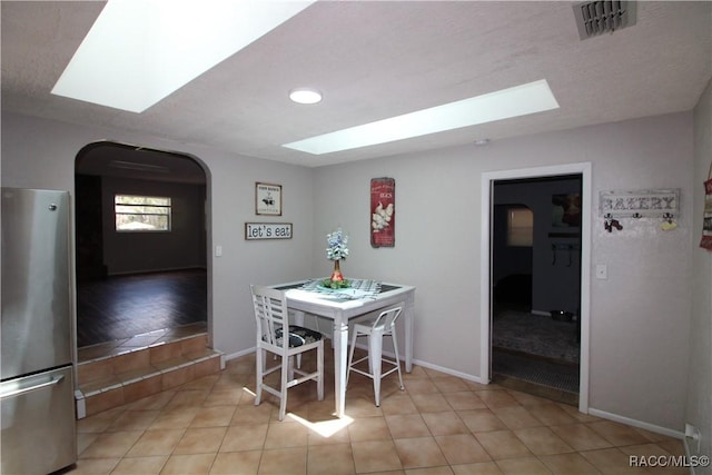 dining room with arched walkways, visible vents, baseboards, and a skylight