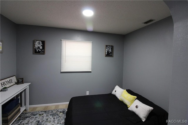 bedroom with a textured ceiling, arched walkways, visible vents, and baseboards