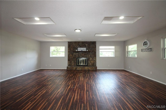 unfurnished living room with dark wood-style floors, a stone fireplace, and plenty of natural light