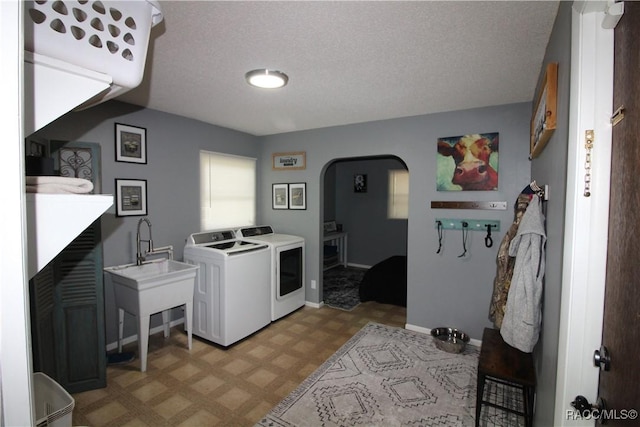 laundry area featuring arched walkways, light floors, washing machine and dryer, a textured ceiling, and laundry area