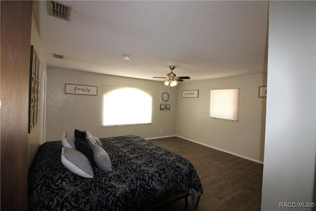 bedroom with ceiling fan, a textured ceiling, dark wood-type flooring, visible vents, and baseboards