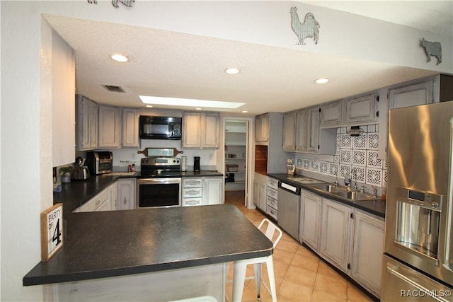 kitchen with stainless steel appliances, dark countertops, a sink, and gray cabinetry