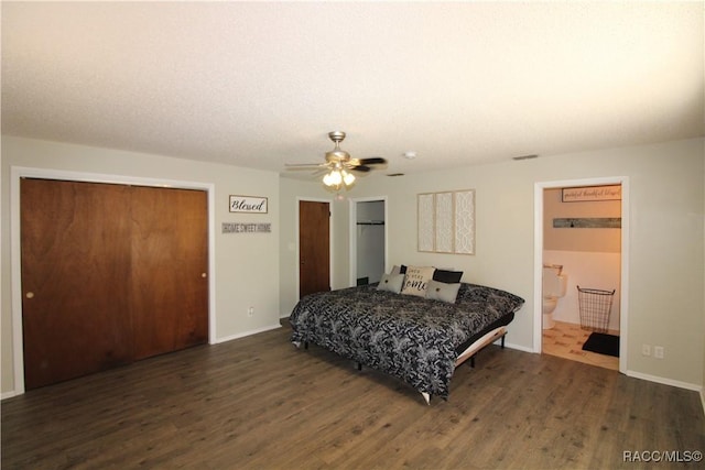 bedroom with ensuite bath, a ceiling fan, dark wood finished floors, and multiple closets