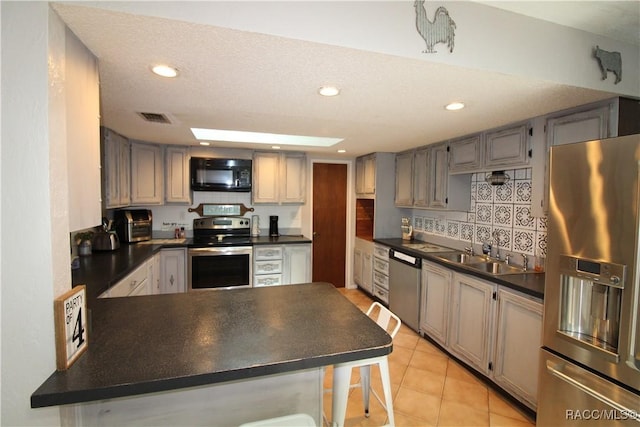 kitchen featuring dark countertops, visible vents, gray cabinetry, appliances with stainless steel finishes, and a sink