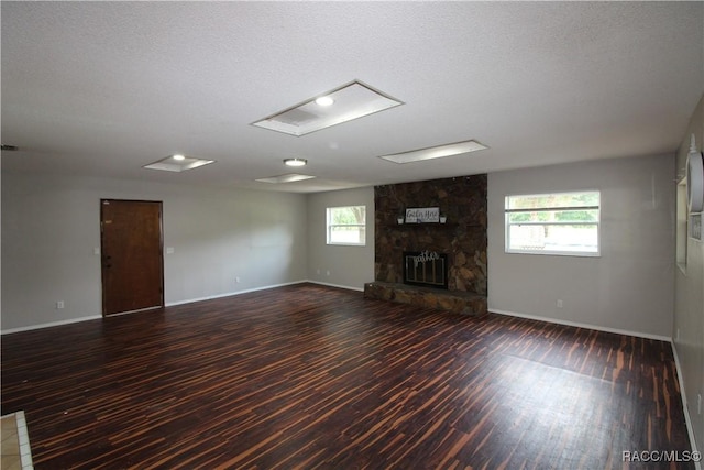 unfurnished living room with a healthy amount of sunlight, baseboards, dark wood-type flooring, and a stone fireplace