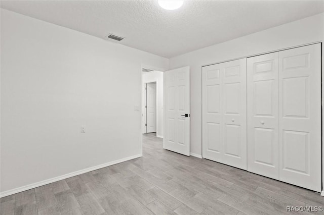 unfurnished bedroom featuring a textured ceiling, baseboards, visible vents, and light wood-type flooring