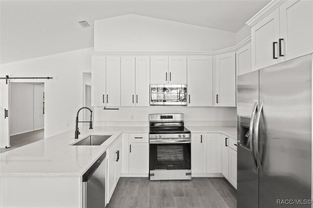 kitchen featuring lofted ceiling, a barn door, appliances with stainless steel finishes, a peninsula, and a sink