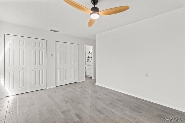 unfurnished bedroom featuring visible vents, baseboards, multiple closets, wood finished floors, and a ceiling fan