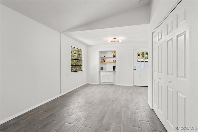 unfurnished room with vaulted ceiling, plenty of natural light, baseboards, and dark wood-style flooring