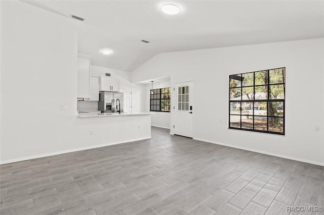 unfurnished living room featuring visible vents, baseboards, lofted ceiling, and wood finished floors