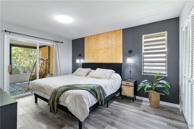 bedroom with access to outside, a textured ceiling, baseboards, and wood finished floors