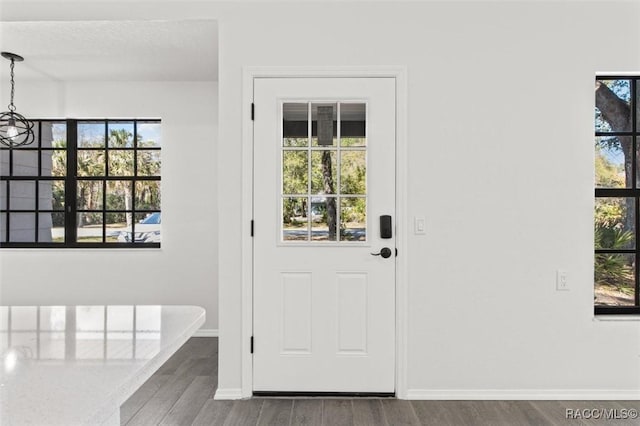 doorway with baseboards, a textured ceiling, an inviting chandelier, and wood finished floors