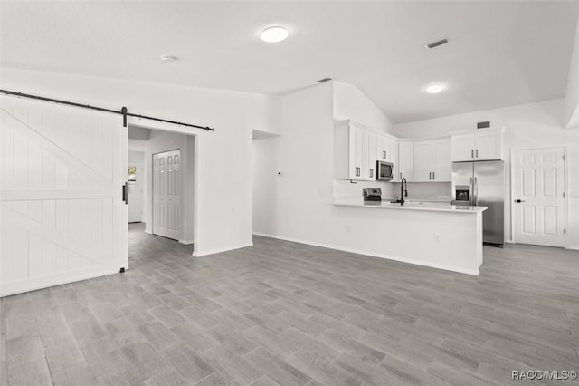 kitchen with open floor plan, light countertops, lofted ceiling, a barn door, and appliances with stainless steel finishes