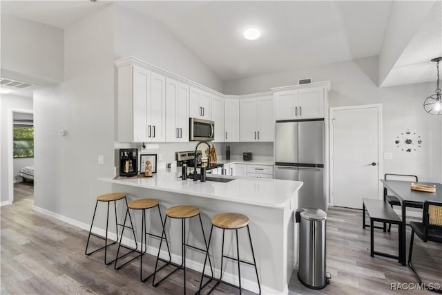 kitchen featuring visible vents, a peninsula, a sink, stainless steel appliances, and a kitchen breakfast bar