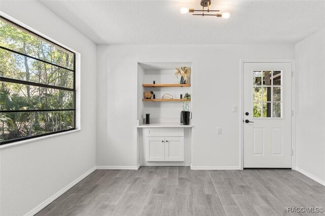 unfurnished dining area featuring an inviting chandelier, light wood-type flooring, and baseboards