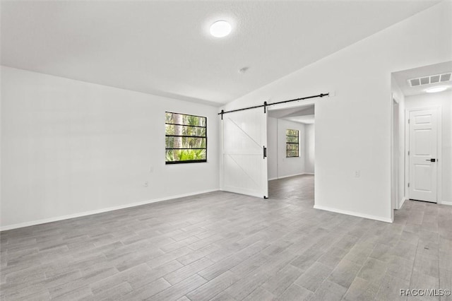 empty room featuring visible vents, baseboards, vaulted ceiling, light wood-style floors, and a barn door