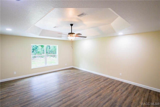 empty room featuring a textured ceiling, ceiling fan, a raised ceiling, and dark wood-type flooring