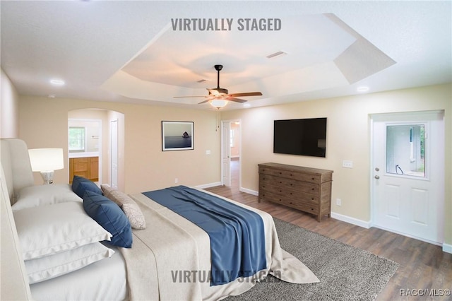 bedroom with hardwood / wood-style floors, ceiling fan, a raised ceiling, and ensuite bath