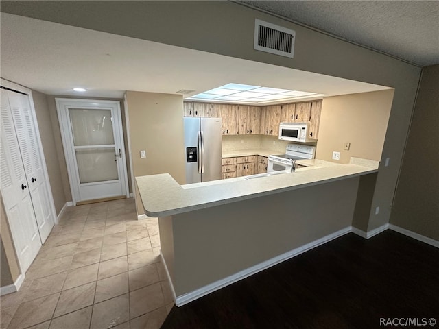 kitchen featuring tasteful backsplash, kitchen peninsula, light tile patterned floors, and white appliances